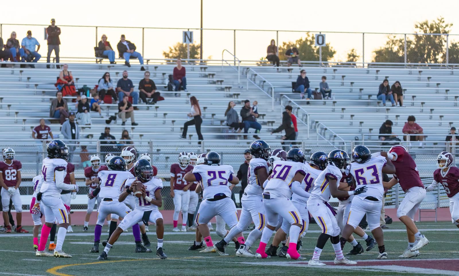 fans in short sleeves in the bleachers at a high school football game at night / high school stadium lights glowing on a mild autumn evening / crowd in a small town stadium under floodlights in fall