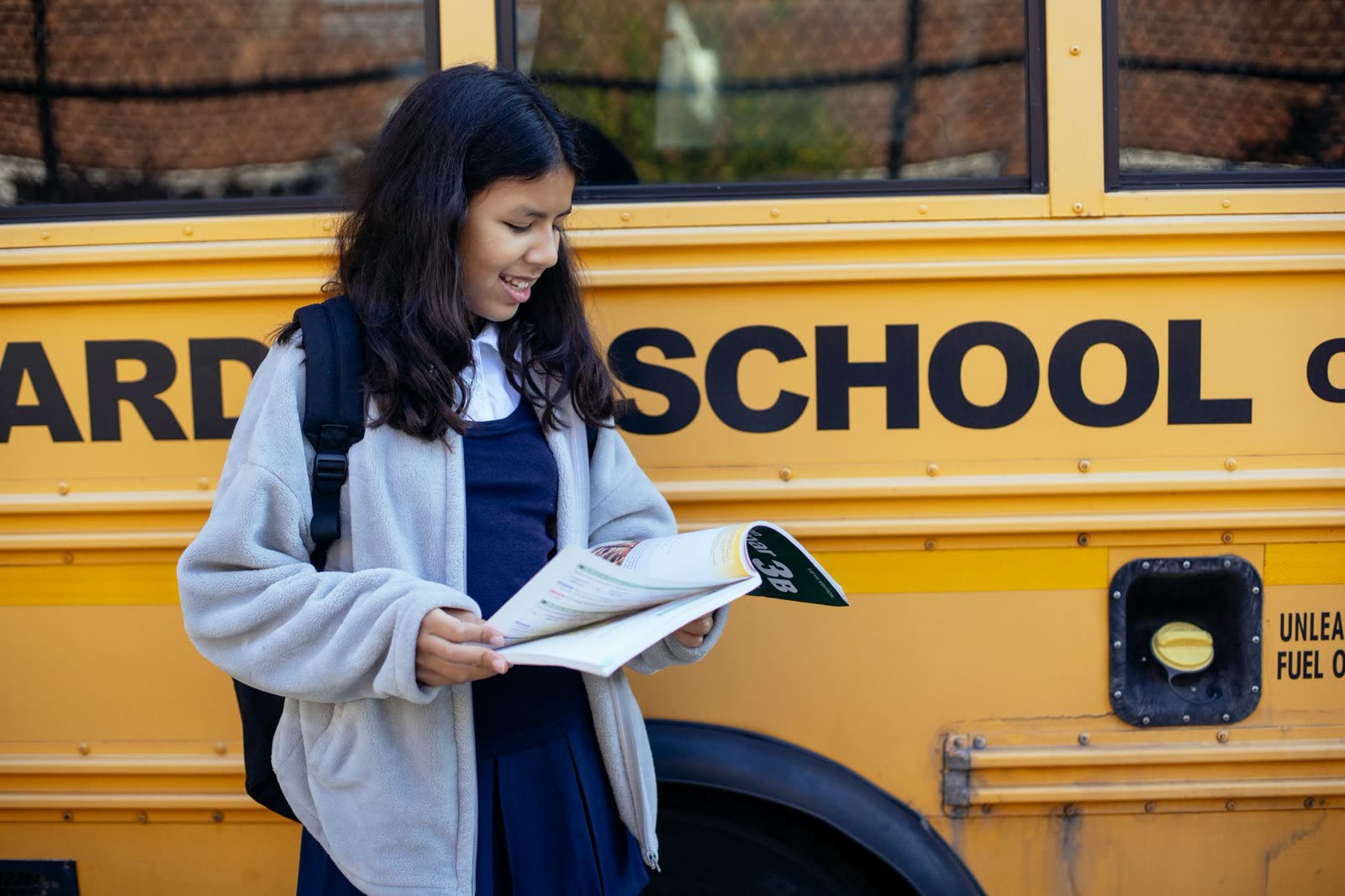 children in hoodies with backpacks waiting at a bus stop on a cool morning / kids waiting for the school bus at sunrise in autumn / yellow school bus on a tree-lined street on a clear fall morning