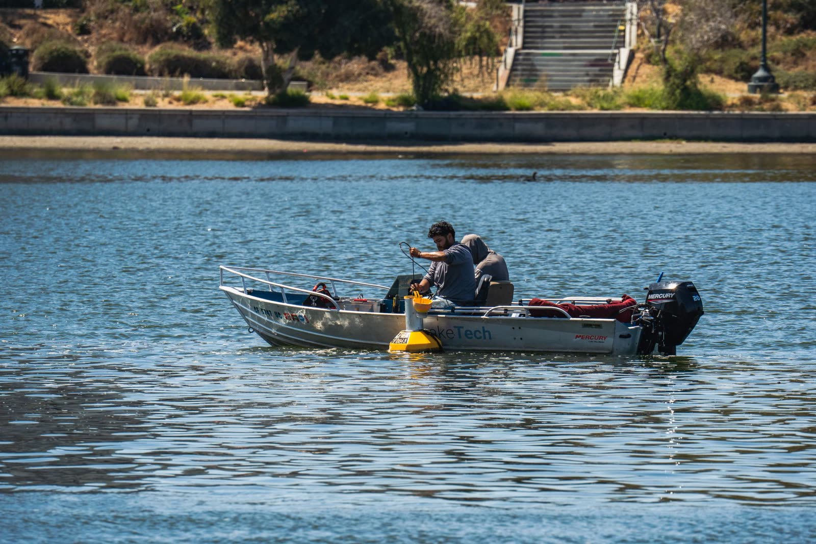 anglers in a small boat on calm water on a sunny fall day / family sitting on a lake dock in autumn sunshine / quiet reservoir with light ripples under a clear sky