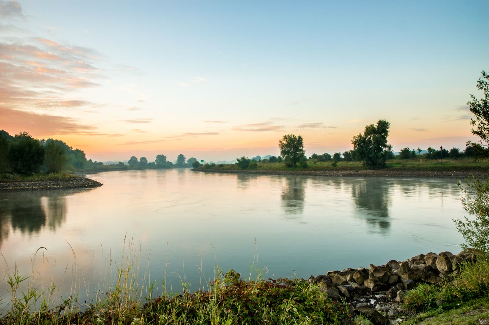 people in short sleeves walking a sunny riverside trail in early autumn / clear blue sky over a small southern town on a warm afternoon / sunrise over a calm river with dry grass along the banks