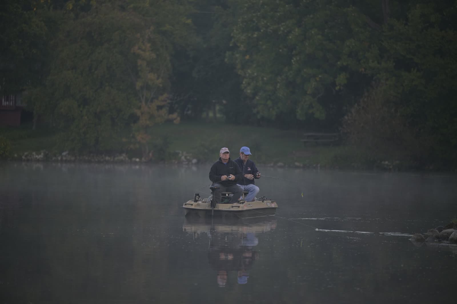 two anglers in a small boat on a calm lake on a cool autumn morning / family sitting on a wooden lake dock in fall / calm lake water under a cloudy autumn sky