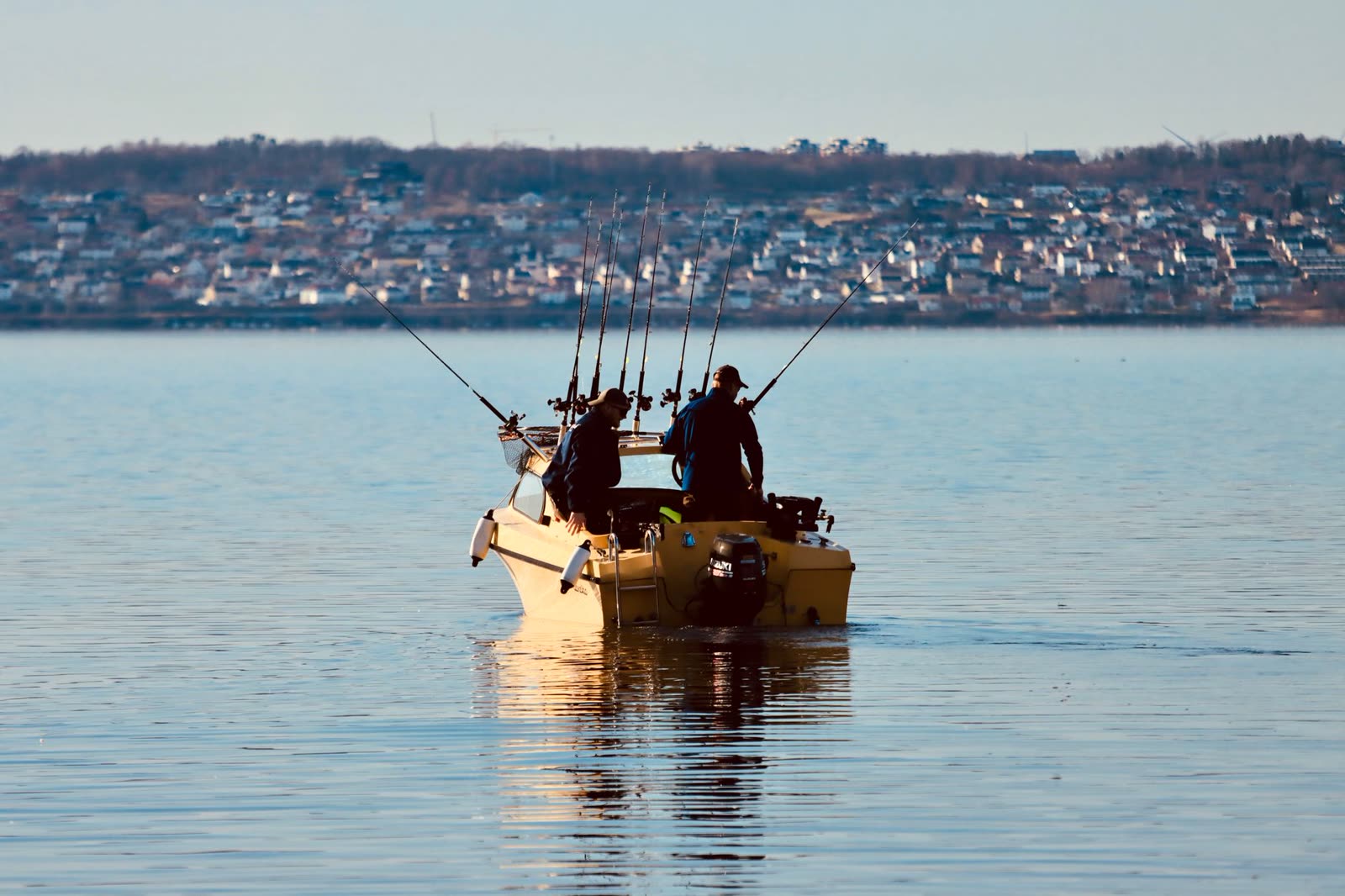 two anglers in a small boat on glassy calm lake water at sunrise / people sitting on a wooden dock on a sunny late summer morning / calm lake with pine trees and clear blue sky