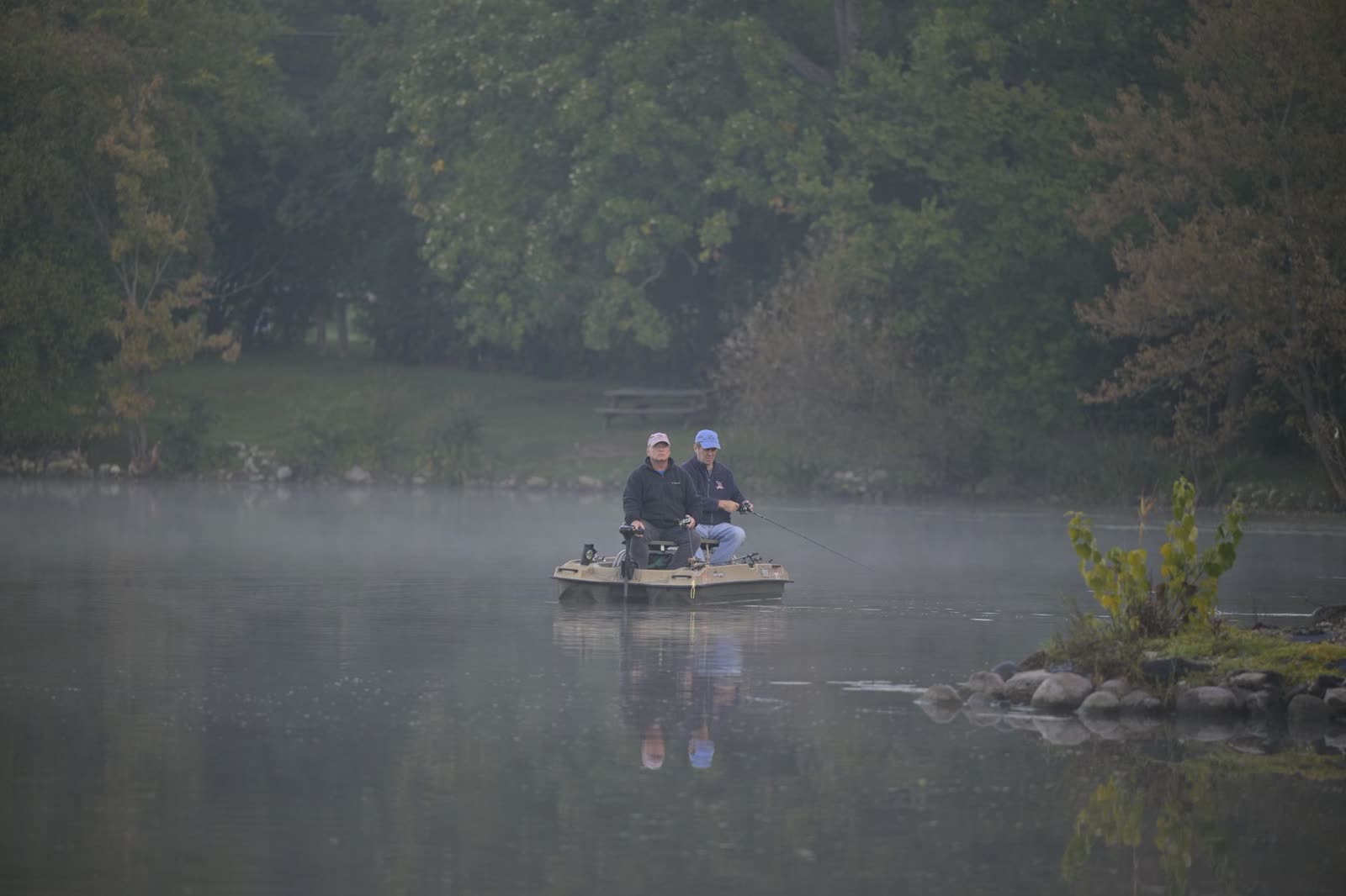 anglers in a small boat on glassy lake water at sunrise / family sitting on a lake dock on a sunny early fall morning / calm lake at dawn with mist rising in early autumn