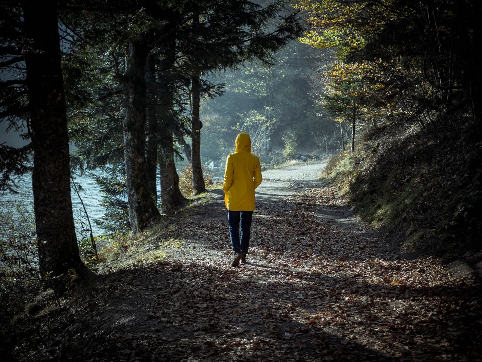 people in light jackets walking a riverside trail on a cool fall morning / low gray clouds over a small southern downtown / sunrise breaking through clouds over a river walking path